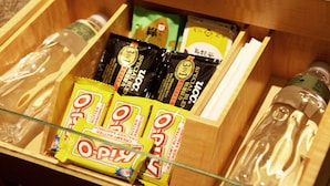 Een houten lade met verschillende etenswaren, waaronder zakjes O-Pop en andere snacks.