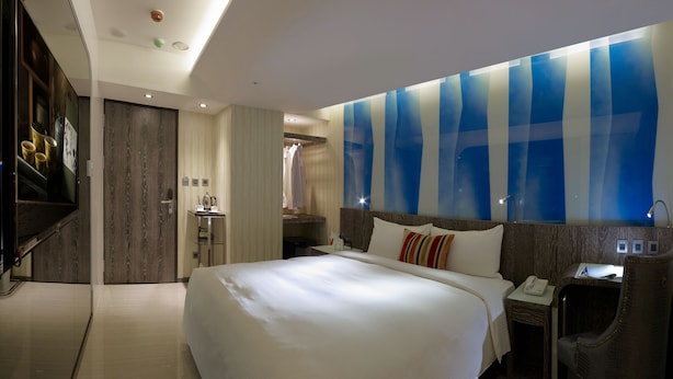 Een moderne hotelkamer met een groot bed, een bureau, een stoel en een badkamer zichtbaar door een geopende deur.