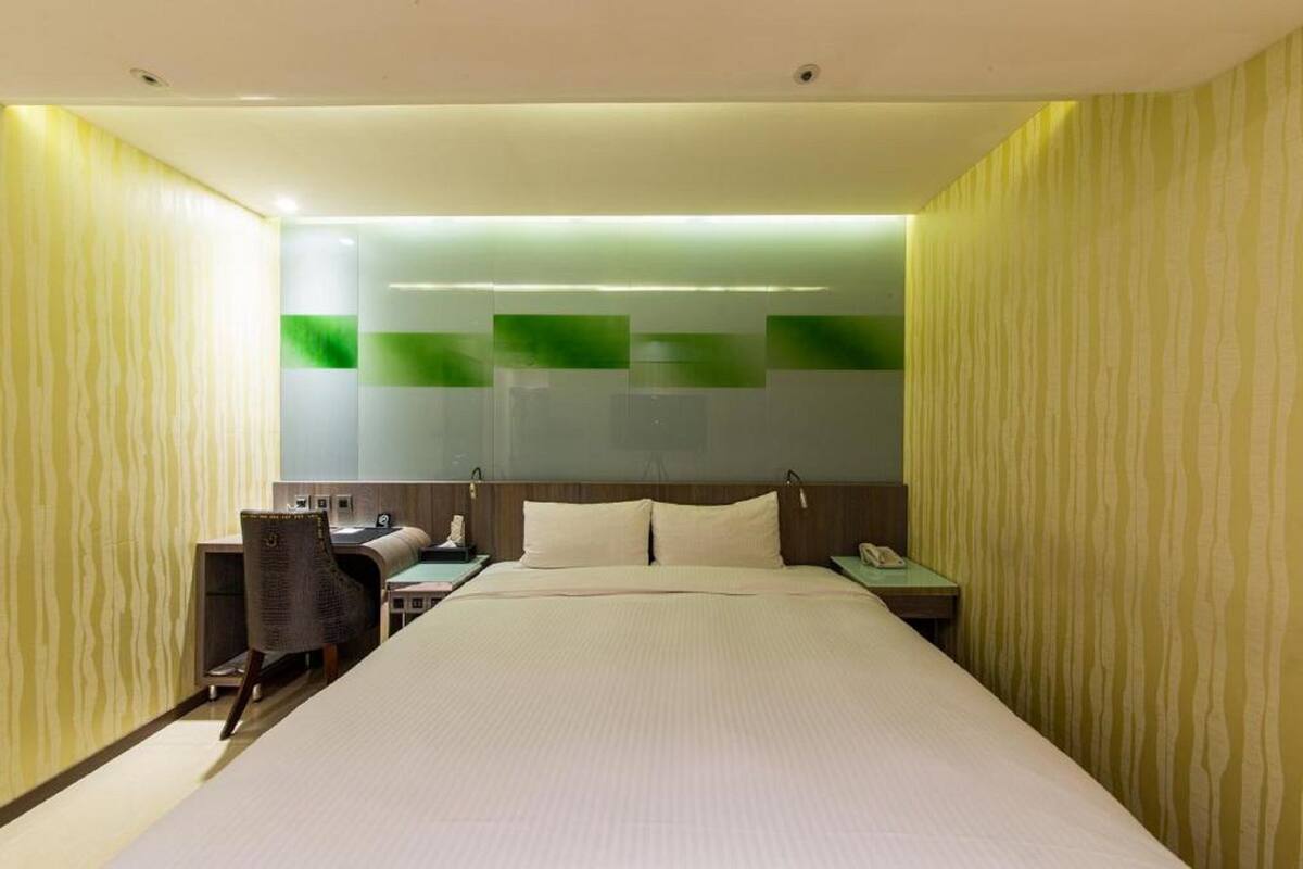 Ein Hotelzimmer mit einem großen Bett, einem Schreibtisch mit Stuhl, einem Telefon und einem Nachttisch.