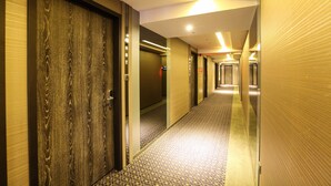 Een hotelgang met houten deuren, een kamerkleed met patroon en een modern lichtplan.
