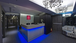 Een hotel lobby met een receptiebalie, een kroonluchter, een bank en een bord met een nooduitgang.'