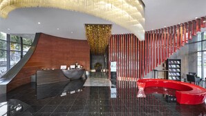Eine moderne Lobby mit einer gebogenen Rezeption, einer roten Sitzecke und einer großen, beleuchteten Deckeninstallation.