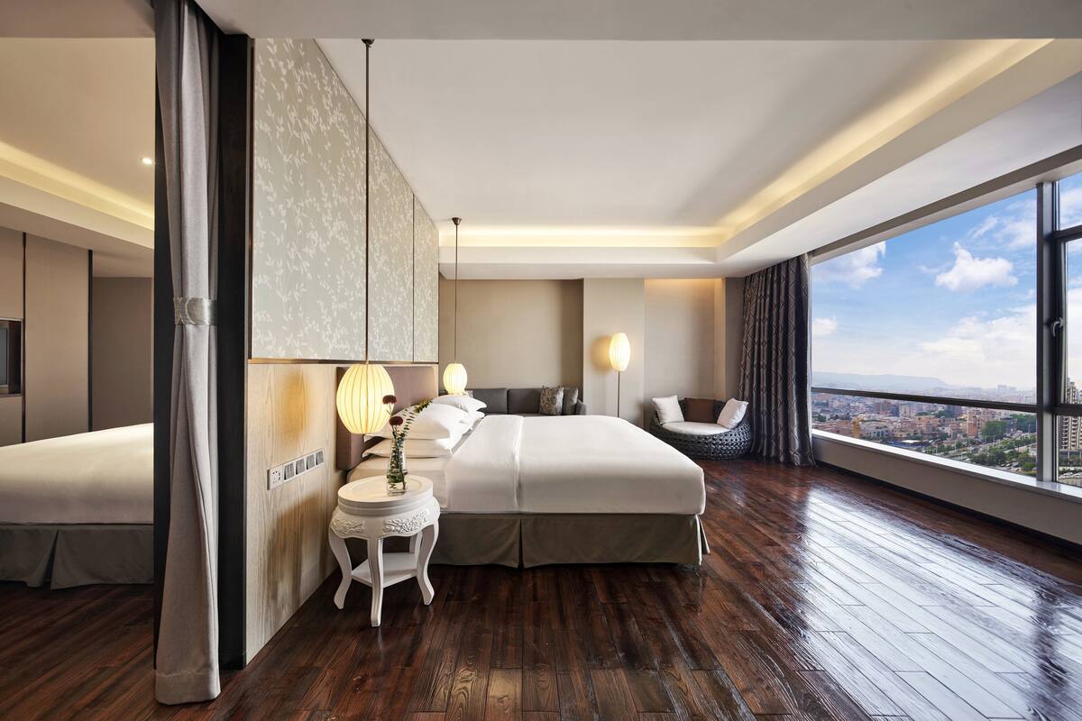 A modern hotel room with a large bed, a seating area, and a city view.