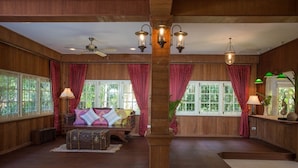 A spacious room with wooden paneling, a large window with red curtains, a ceiling fan, and a wooden bench with cushions. - Baan Khun Nang Colonial Residence (Koh Samui)
