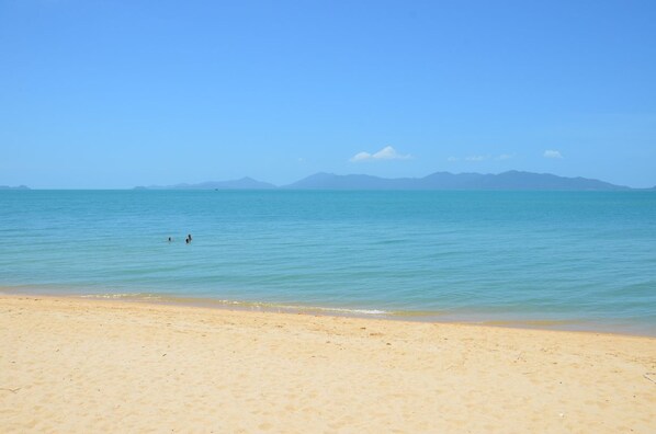 A beach with clear blue water and distant mountains.