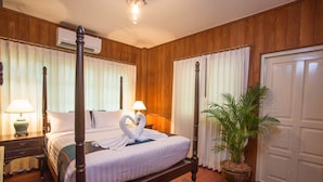 A four-poster bed with a heart-shaped towel arrangement, a potted plant, and a wooden nightstand with a lamp. - Baan Khun Nang Colonial Residence (Koh Samui)