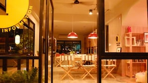 Un interior moderno con entrada por puerta de cristal, un comedor con mesas y sillas, y un ventilador de techo.