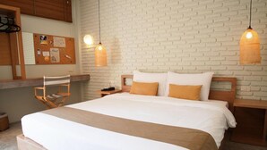 Un dormitorio ordenado con una cama grande, cabecera de madera y dos mesitas de noche. Un tablón de corcho con varios objetos está colgado en la pared sobre la cama.