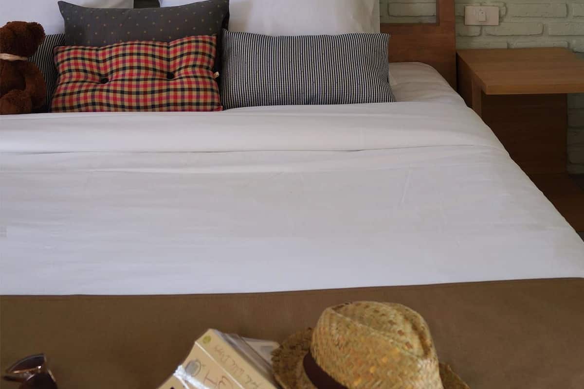 A neatly made bed with a wooden headboard, a wicker hanging light fixture, and a brown bedside table.