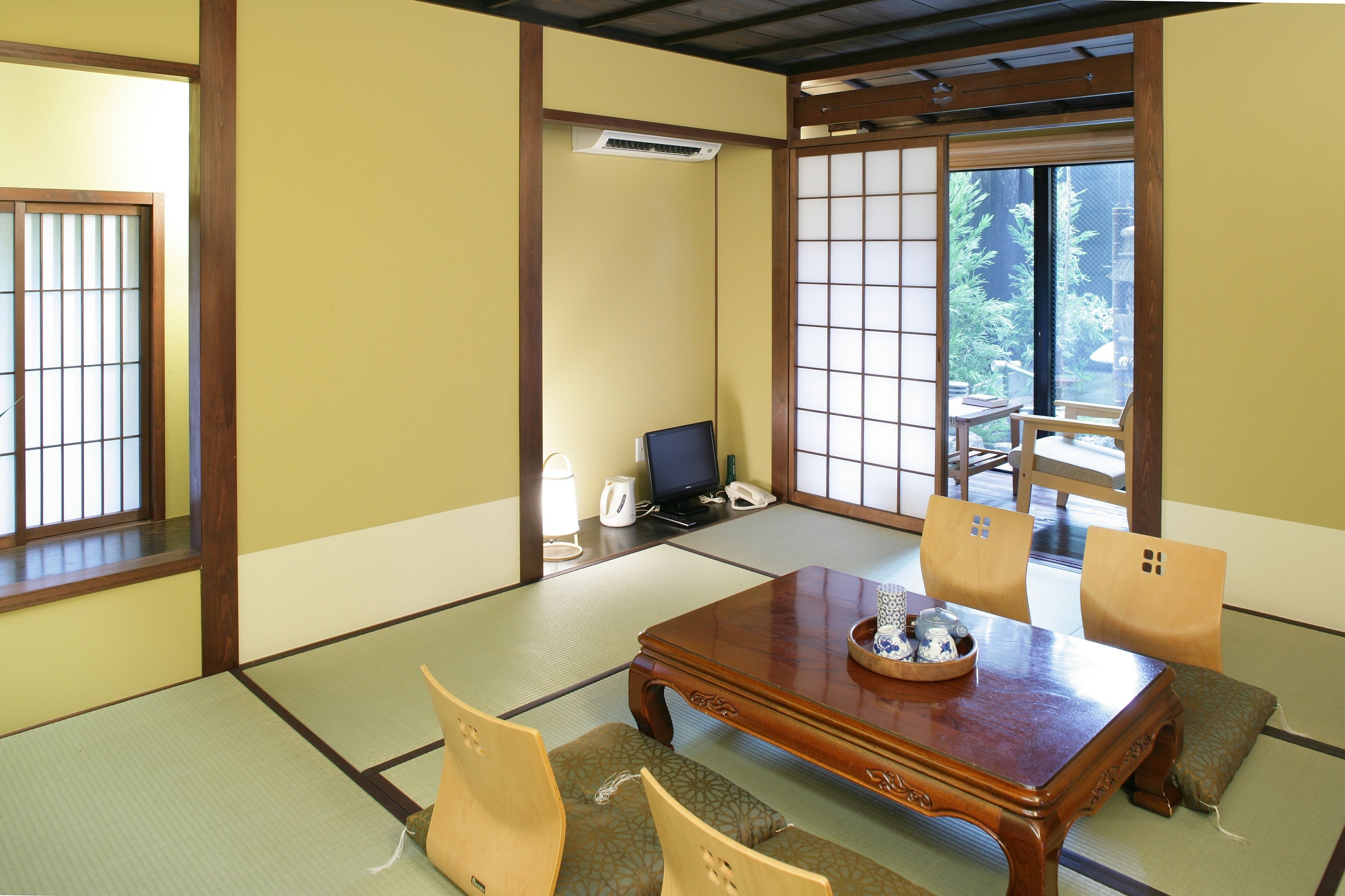 A traditional Japanese room with tatami flooring, a wooden table with cushions, and a sliding door leading to a garden.