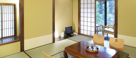 A traditional Japanese room with tatami flooring, a wooden table with cushions, and a sliding door leading to a garden.