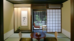 A traditional Japanese room with tatami flooring, a low wooden table, two cushions, a sliding door, and a view of the outside. - Matsubaya Ryokan (Kyoto)