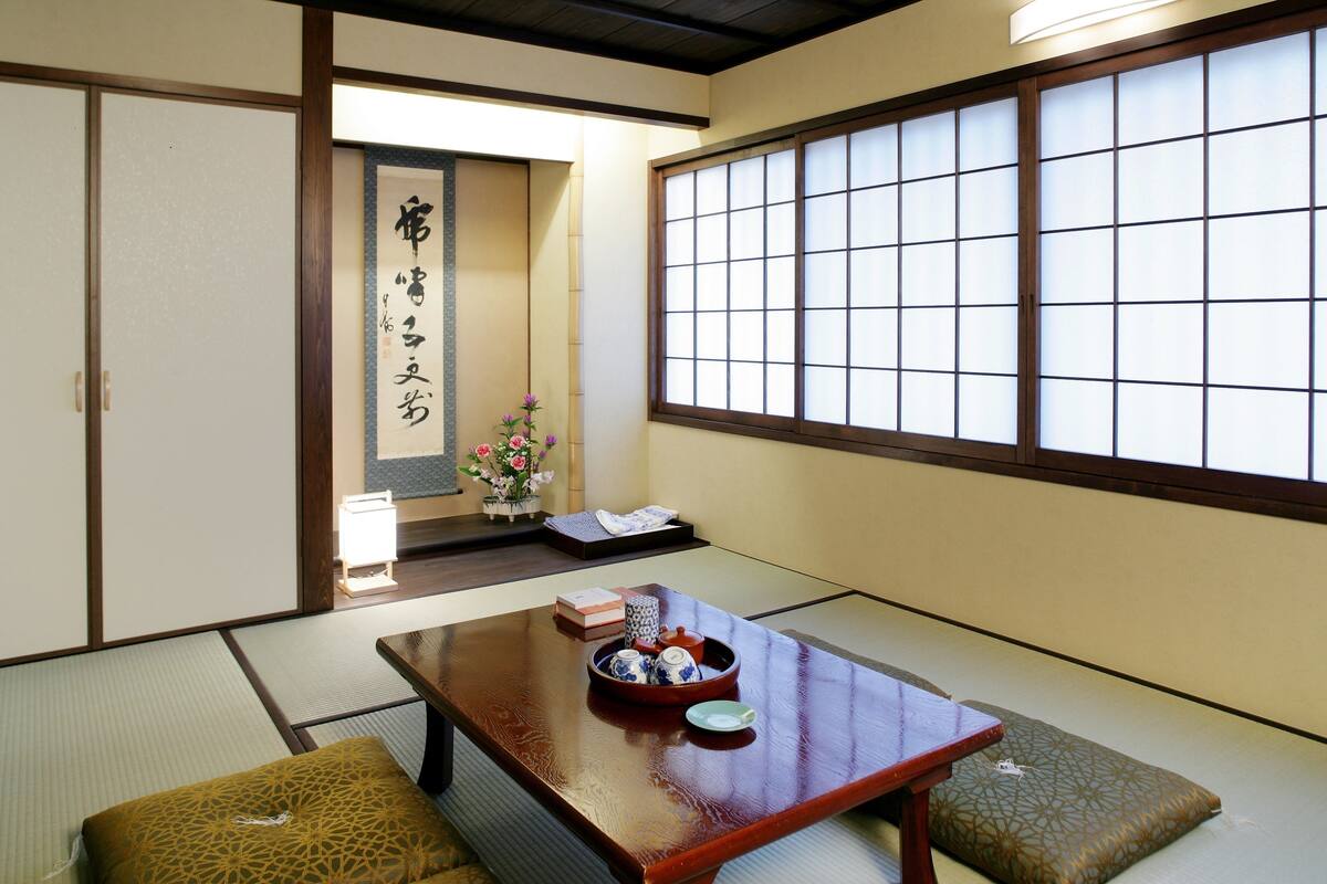 A traditional Japanese room with tatami flooring, a low wooden table with tea set, and a sliding door with calligraphy.
