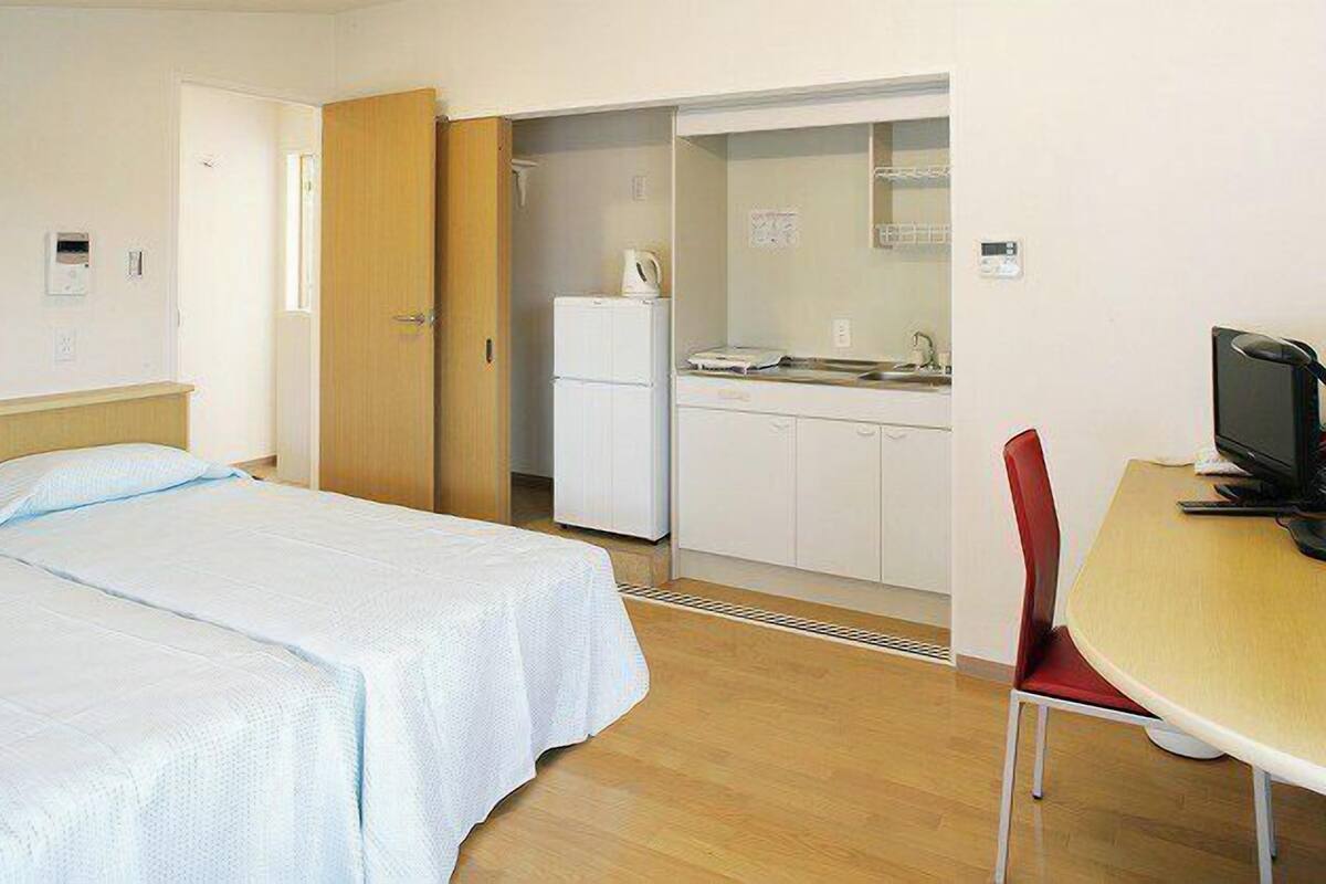 A bedroom with a bed, a small kitchenette, a television, and a chair.