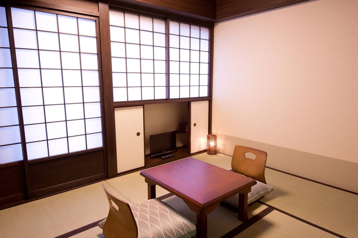 A traditional Japanese room with tatami flooring, a low table, two cushions, and sliding doors with paper partitions.