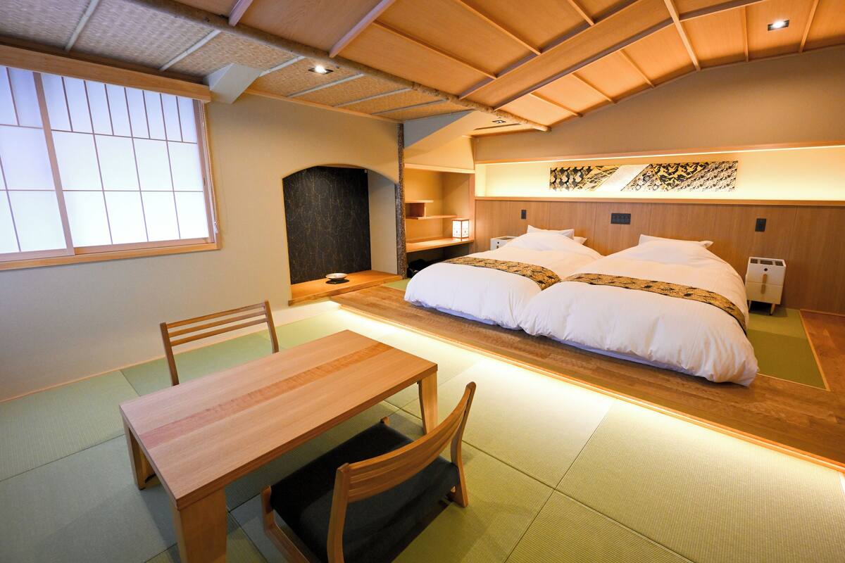 A traditional Japanese-style room with tatami flooring, a low wooden table, and a double bed with white bedding.