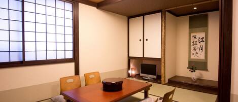 A traditional Japanese room with tatami flooring, a low wooden table, and a television.
