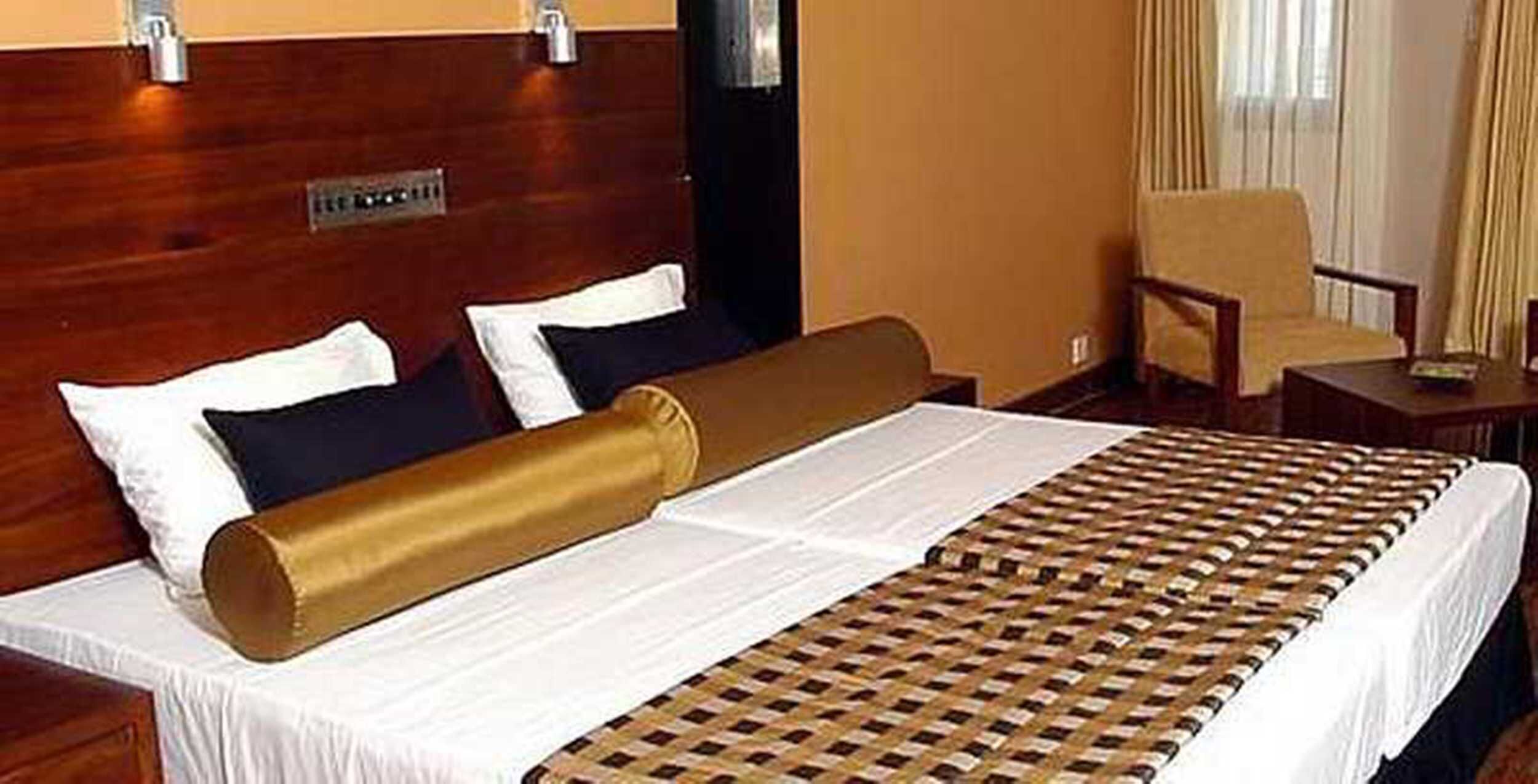 Habitación de hotel con una cama grande, cabecera de madera, una silla y una mesita.