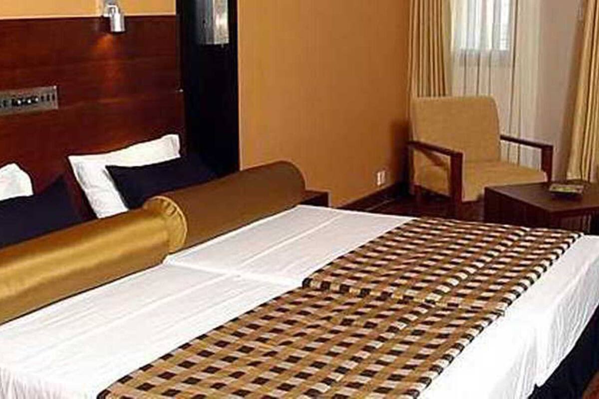 Habitación de hotel con una cama grande, cabecera de madera, una silla y una mesita.