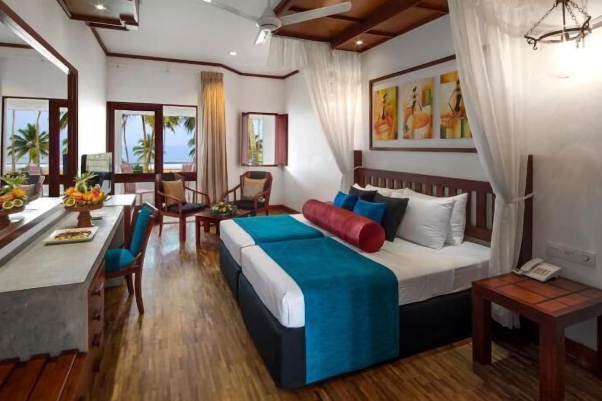 A hotel room with a bed, a desk with a fruit bowl, a chair, a small table, and a phone.
