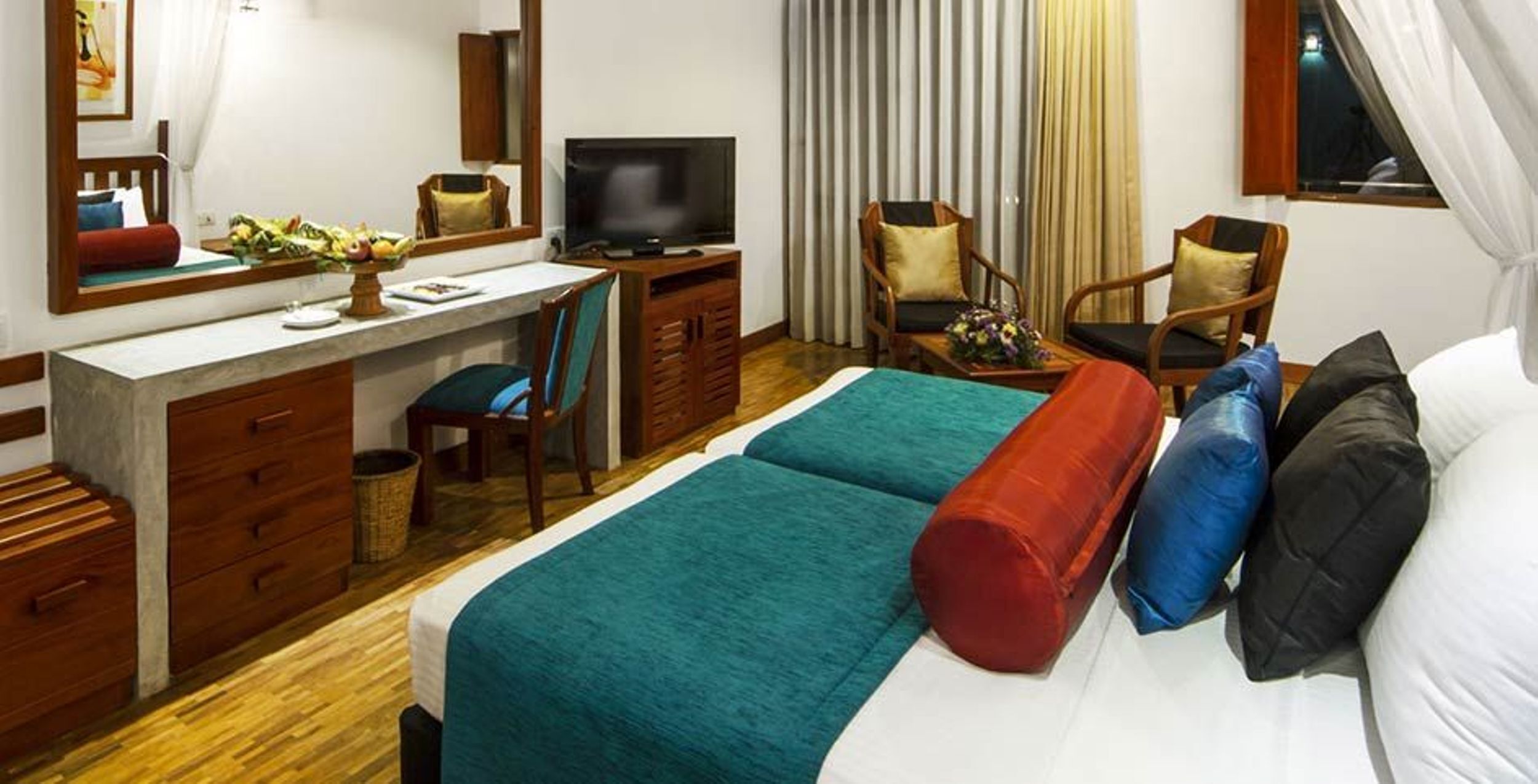 Una habitación de hotel con cama, escritorio, silla, televisor y cortinas.