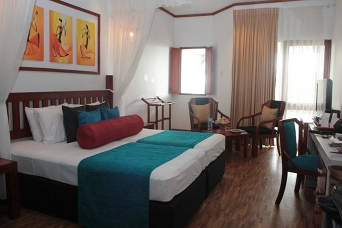 Habitación de hotel con cama, escritorio, silla, televisor y una obra de arte en la pared.