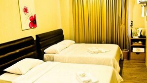 Una habitación de hotel con dos camas, un cabecero negro, un cuadro de flores, una cortina y una mesita de noche con una lámpara y un florero.