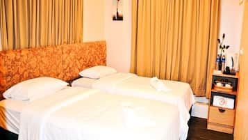 Habitación de hotel con dos camas, cabecero de madera, una mesita de noche de madera con un florero y botellas, y un cuadro colgado en la pared.