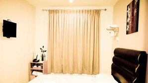 Habitación de hotel con cama, mesita de noche con lámpara, televisor montado en la pared y cortina.