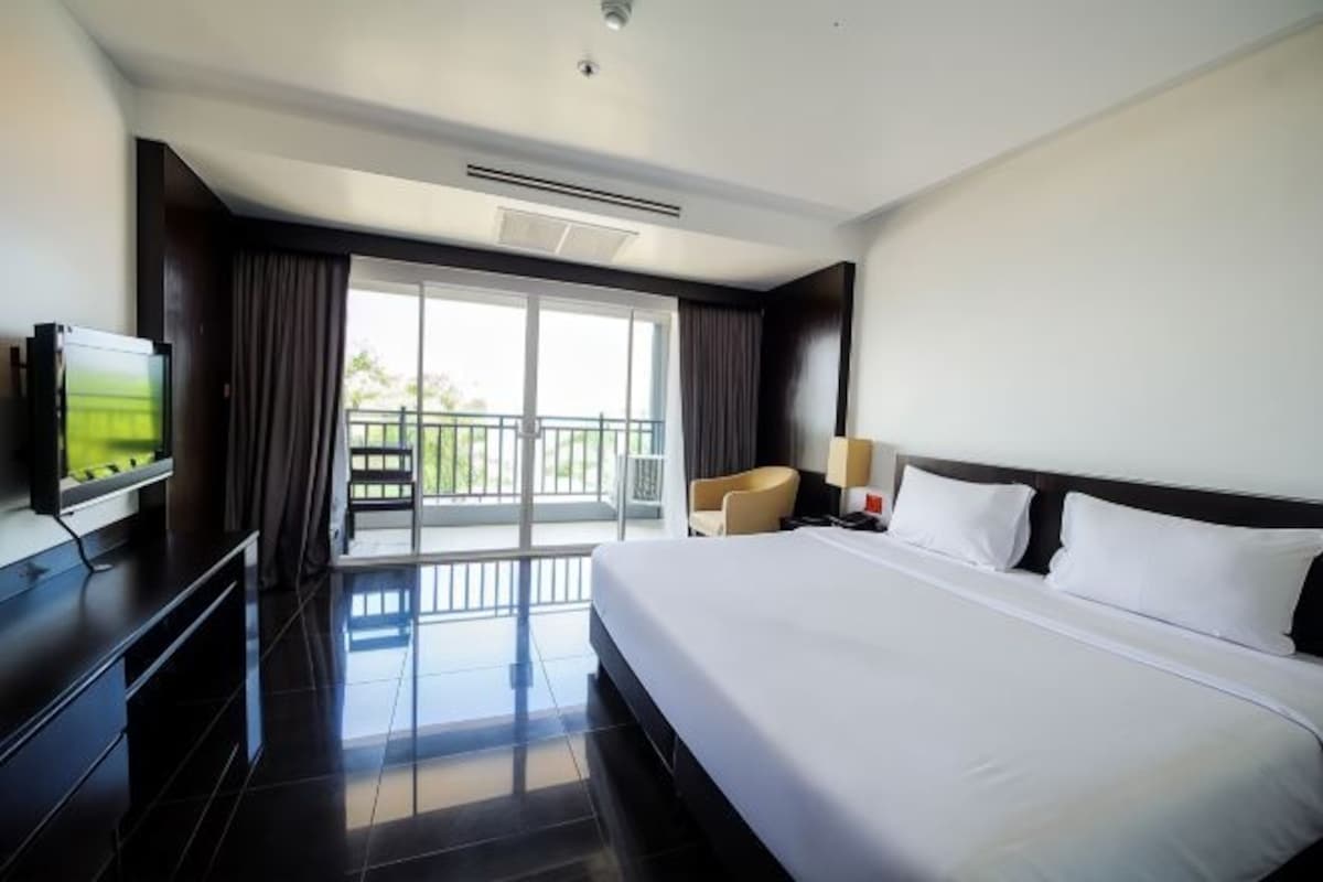 A modern hotel room with a large bed, a flat-screen TV, a balcony with a view, and a seating area.