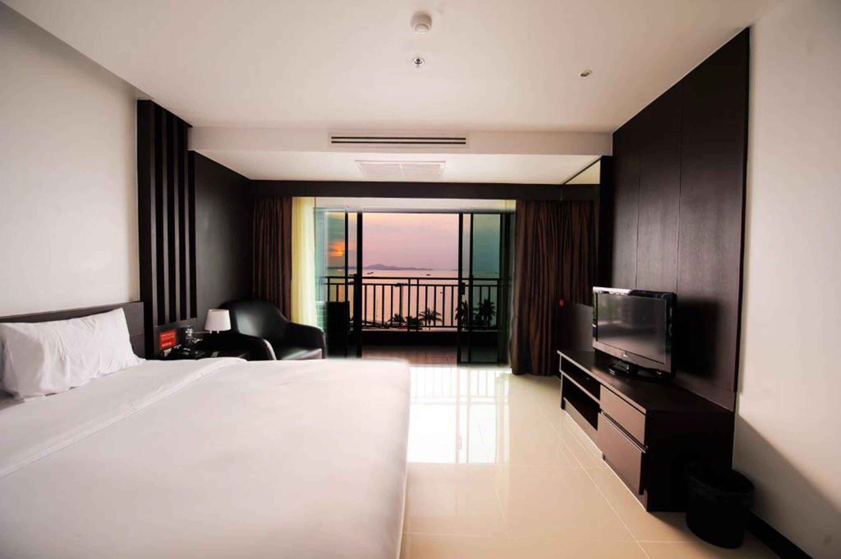 A modern hotel room with a large bed, a TV, a desk, and a balcony with a city view.