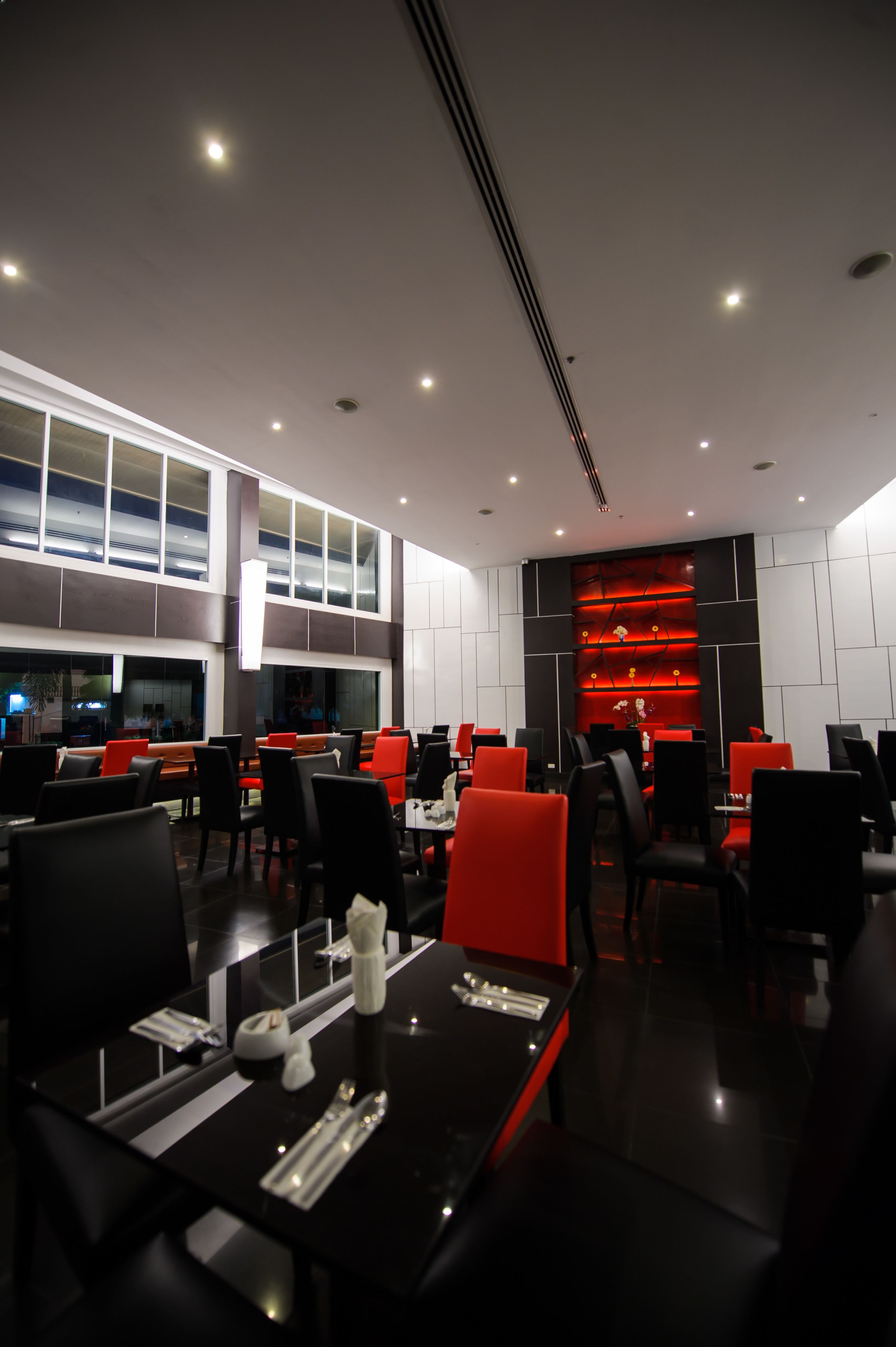 Un restaurant moderne avec des chaises noires et rouges, une table noire et un mur d’accent rouge.