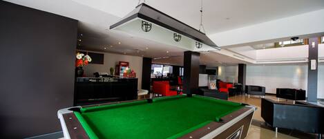 A pool table in a modern indoor setting with a bar area in the background.