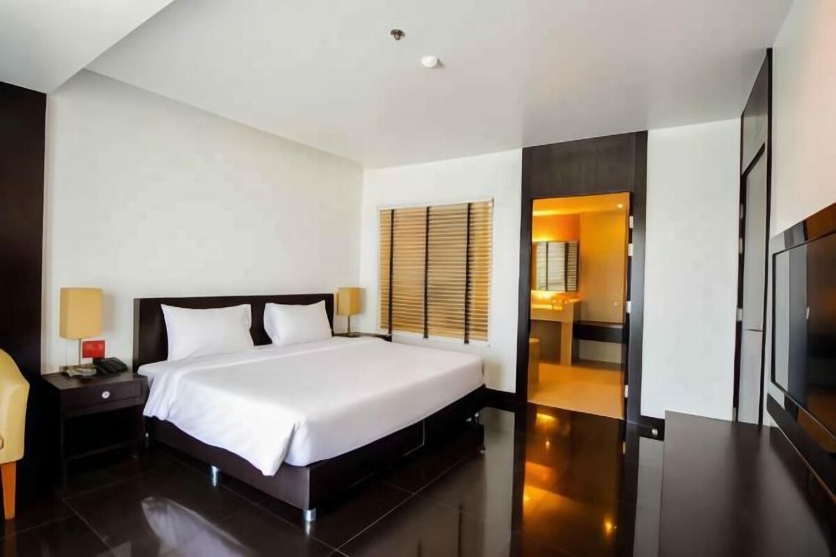 Una habitación de hotel moderna con una cama grande, mesitas de noche, un televisor y un baño visible a través de una puerta abierta.