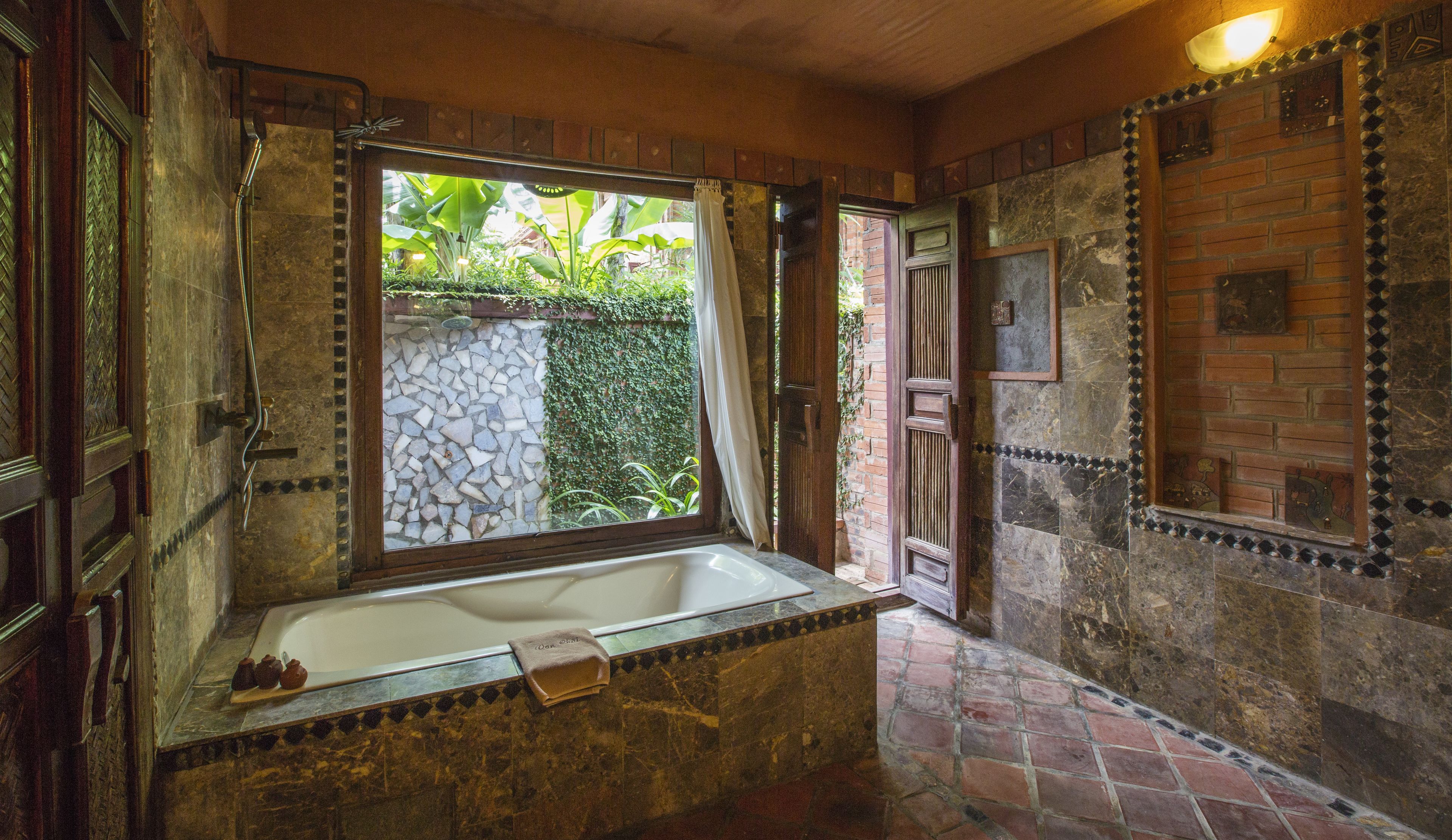 Ein Badezimmer mit einer großen Badewanne, einem Fenster mit Vorhängen und einer Steinwand mit Mosaikbordüre.
