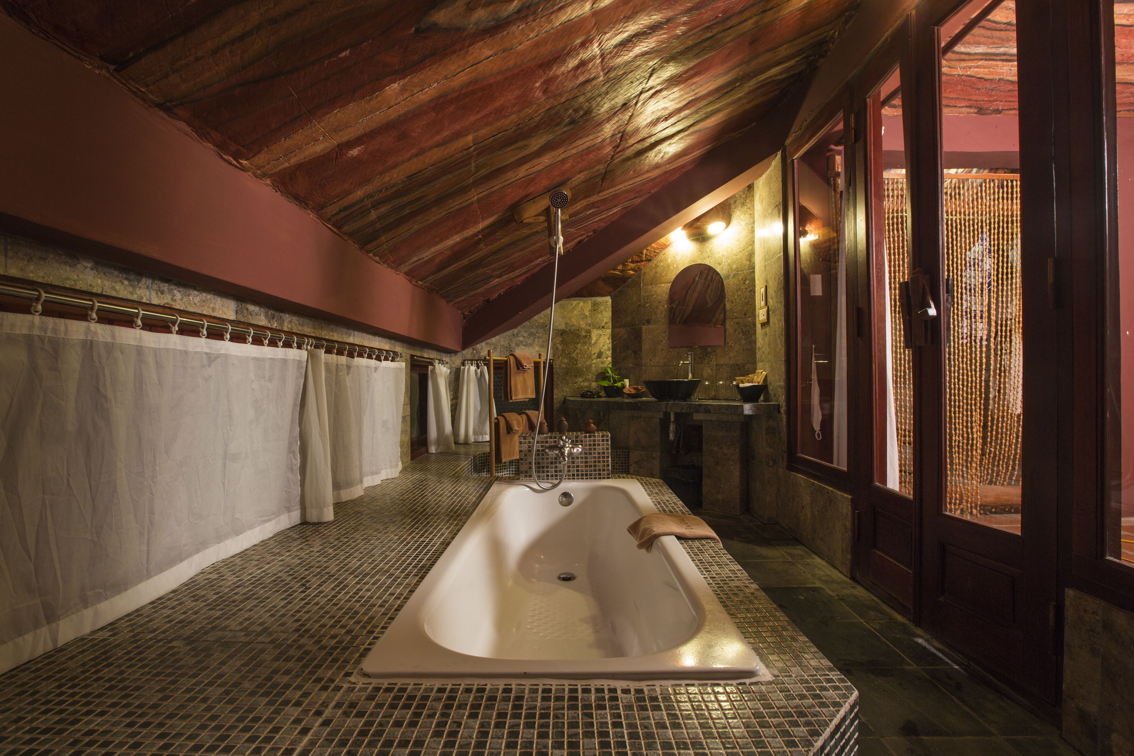 A bathroom with a large bathtub, tiled floor, wooden ceiling, and a sink area with a mirror.