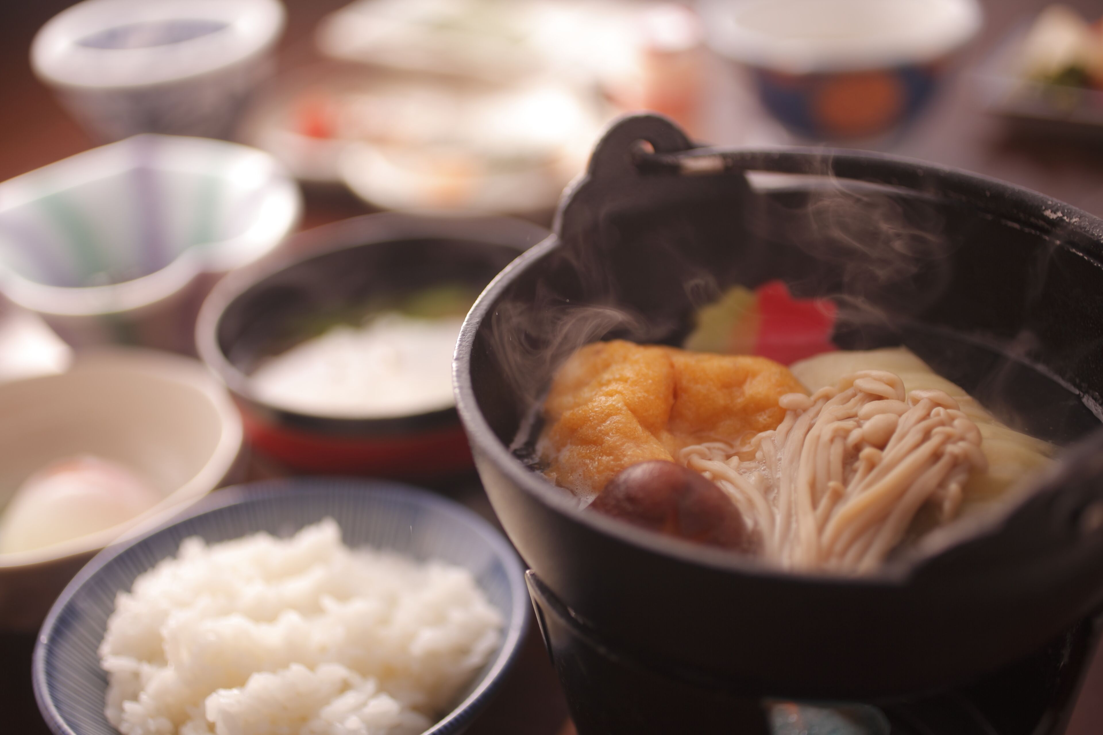 A traditional Japanese hot pot with various ingredients, including tofu and mushrooms, surrounded by bowls of rice and other dishes.