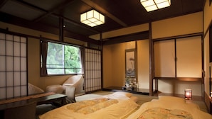 Una habitación tradicional japonesa con suelo de tatami, una cama baja de madera, un escritorio y un ventanal con vistas a zonas verdes.
