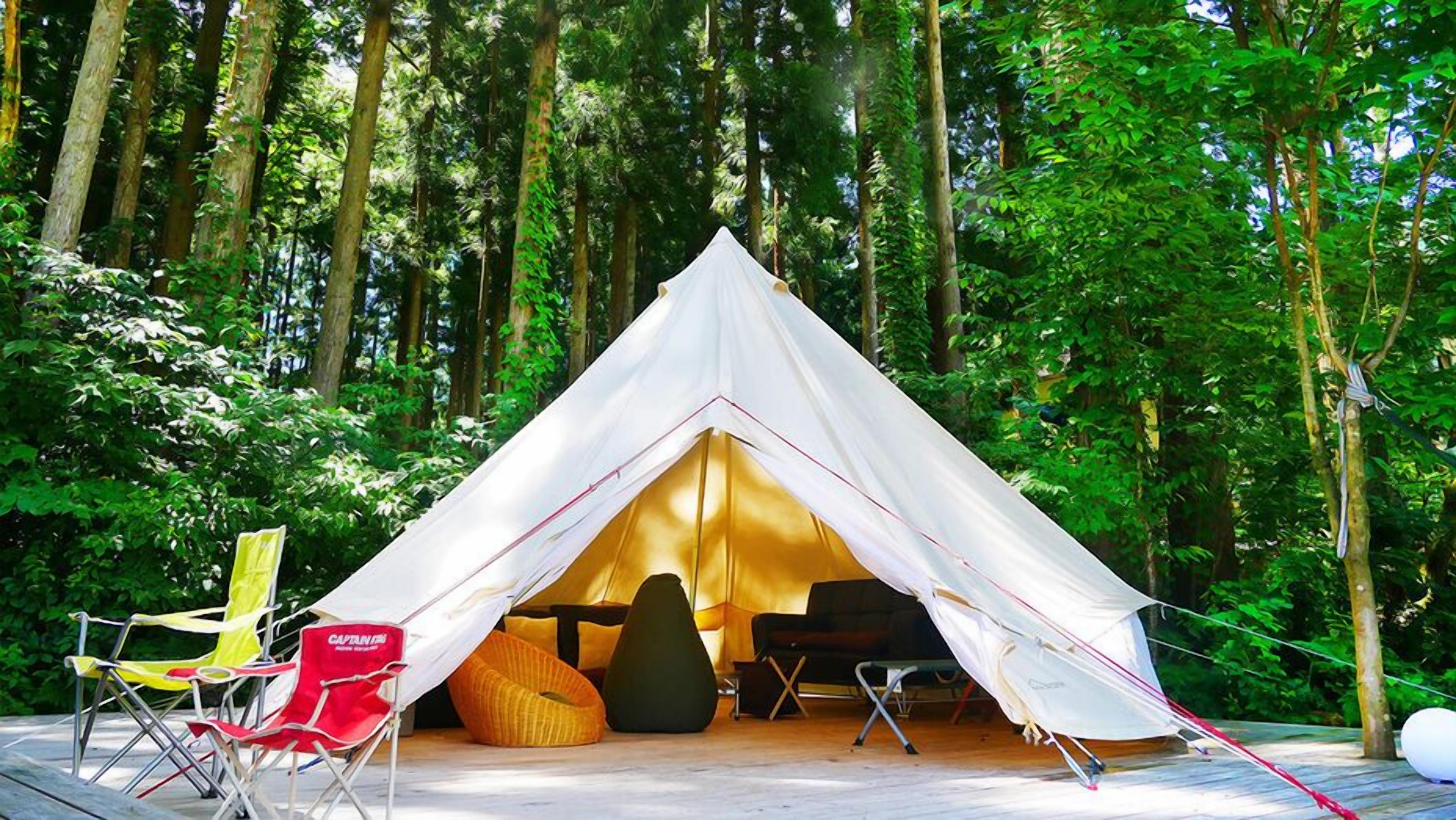 A tent with a table and chairs inside, surrounded by trees.