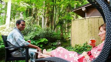 A man and a woman sitting on wicker chairs in a garden with a bamboo fence and lush greenery.
