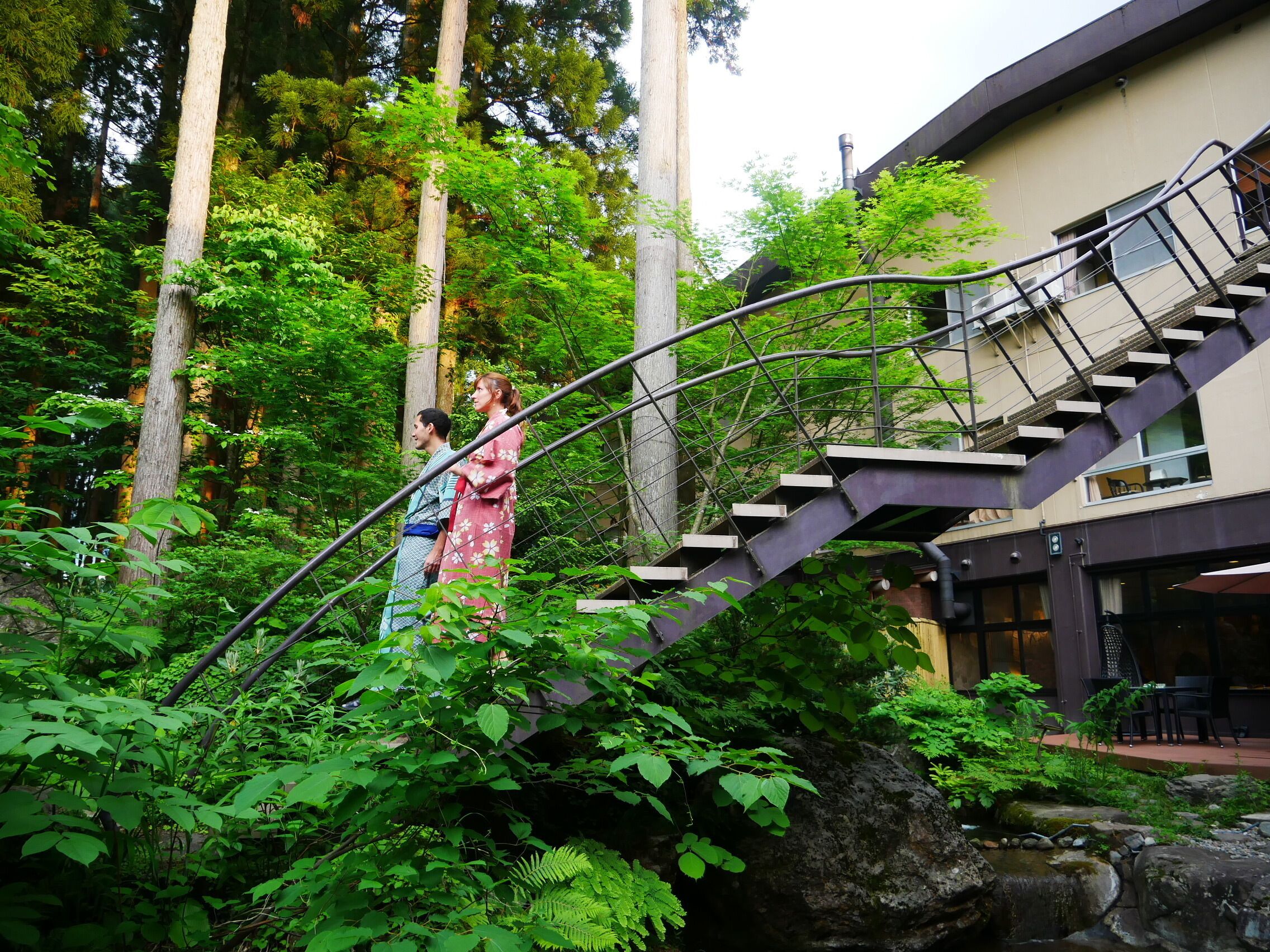 A staircase leading up to a building with a view of a lush garden and tall trees.