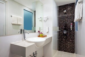 A modern bathroom with a white sink, a mirror, a blue door, and a shower with a patterned tile wall.