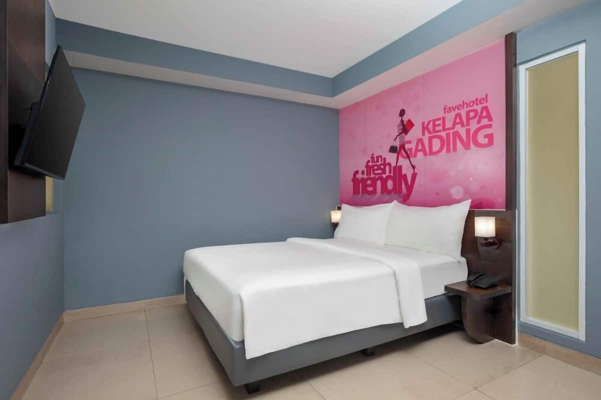 Habitación de hotel con cama, mesitas de noche, televisor y un cartel promocional en la pared.
