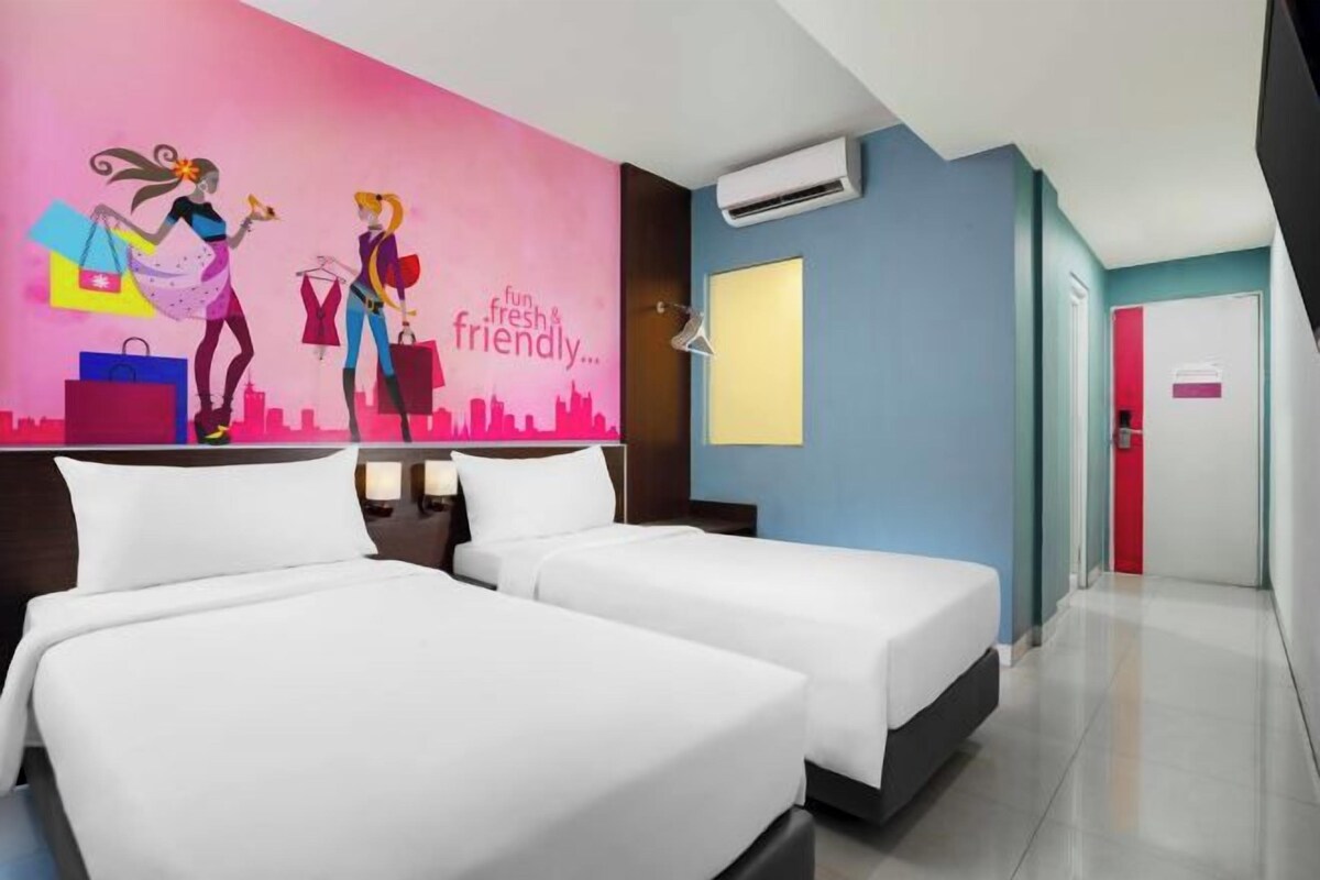 Habitación de hotel con dos camas, un mural de paisaje urbano y una puerta roja.