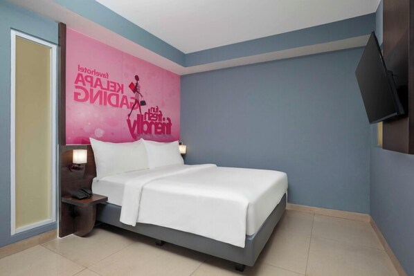 Habitación de hotel con cama, mesita de noche, televisor montado en la pared y un cartel en la pared.