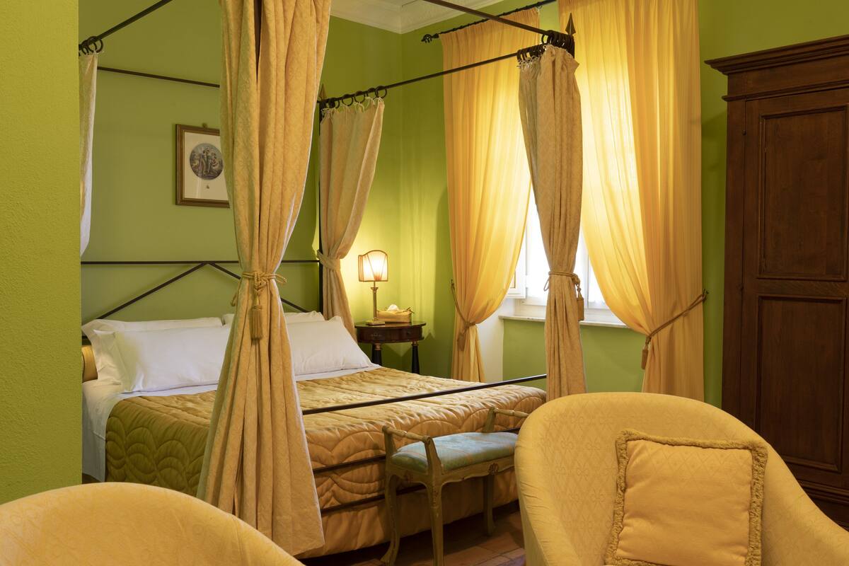 A room with a bed, a bedside table with a lamp, a chair, and a wardrobe.