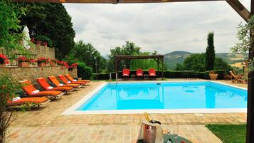A swimming pool with red lounge chairs and a pergola, surrounded by stone walls and greenery.