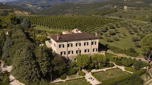 A large, two-story building with a symmetrical facade, surrounded by well-maintained gardens and vineyards.