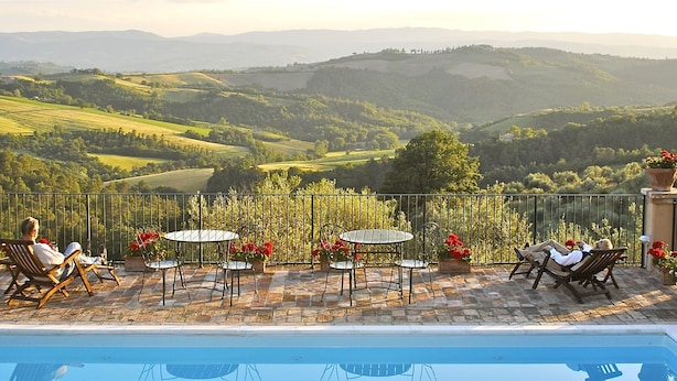 A poolside area with a view of rolling hills, outdoor seating, and potted plants.