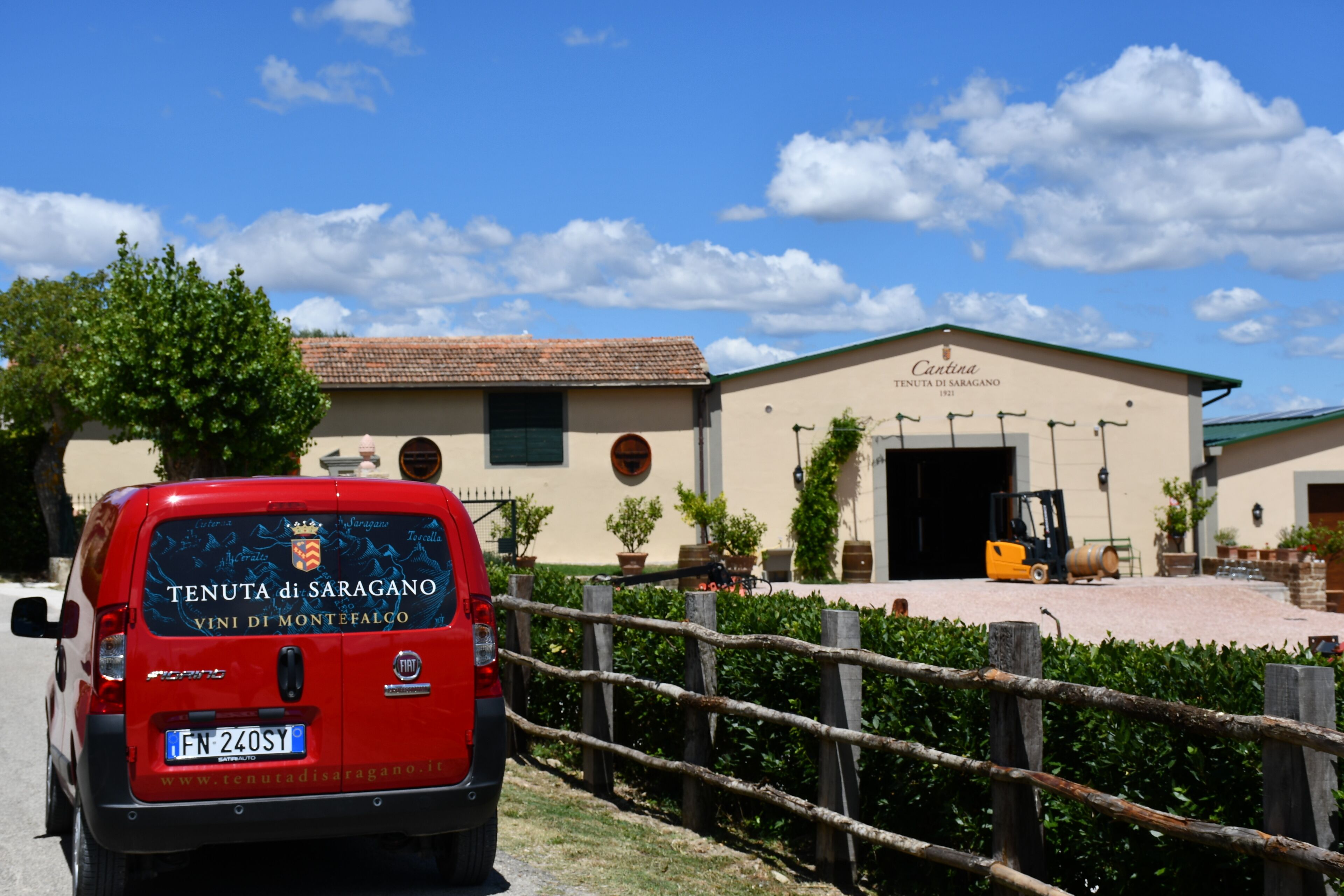 A red van parked in front of a building with a sign reading 'Cantina Tenuta di Saragano 1921'.